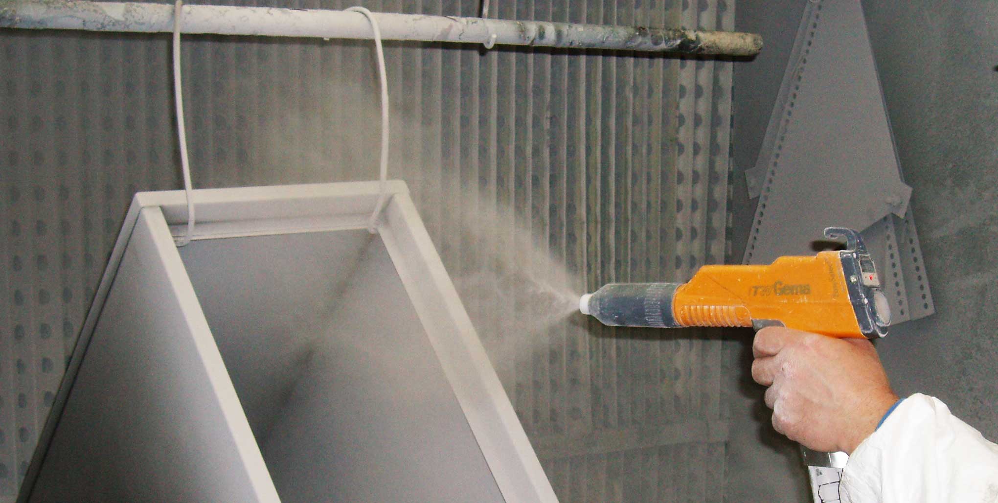 Powder coating applied to a metal frame inside a coating enclosure; a hand holds the application gun.